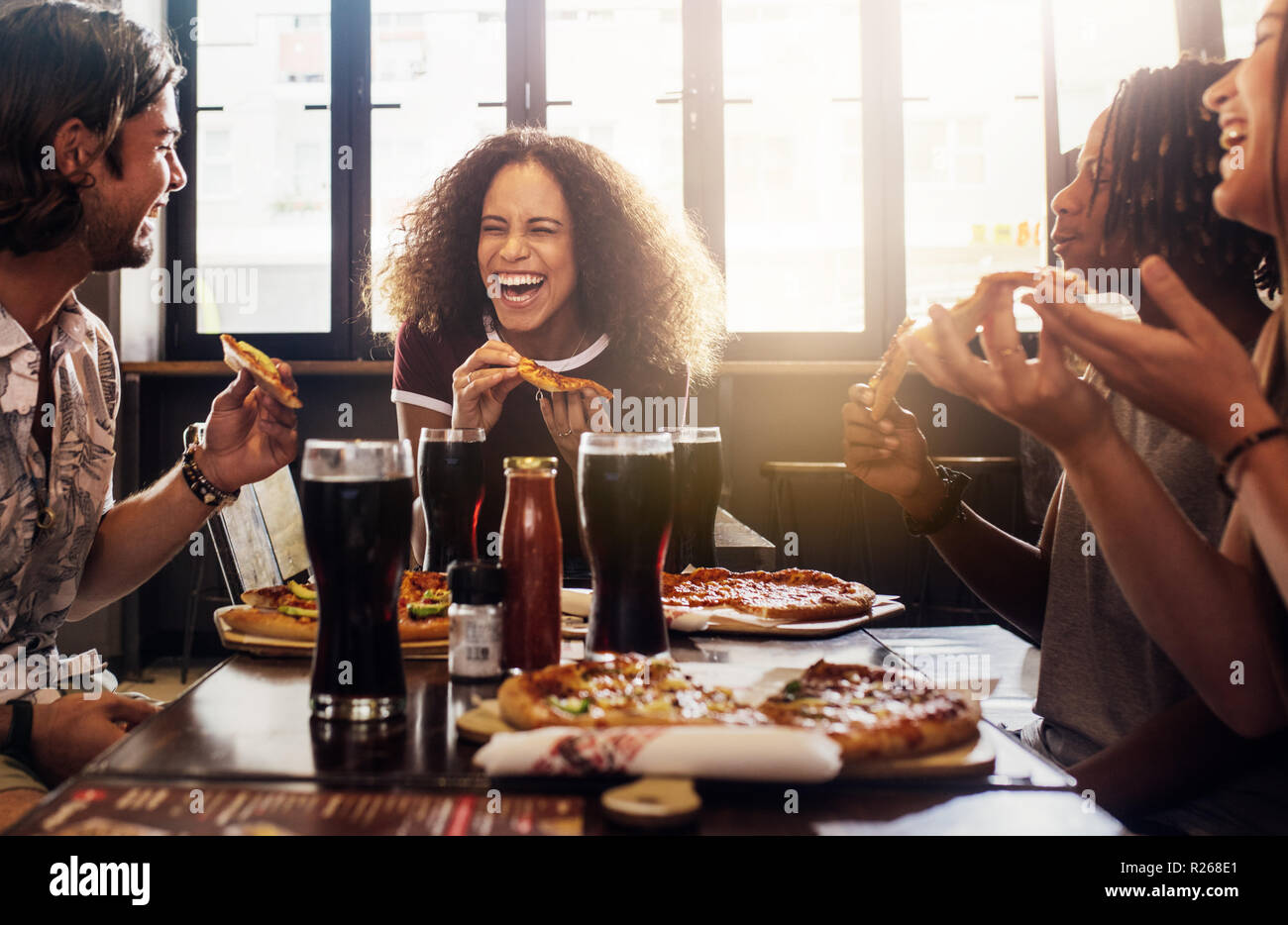 Giovane donna di mangiare la pizza e ridere mentre è seduto con i suoi amici in un ristorante. Gruppo di amici godendo pur avendo il cibo e le bevande presso il cafe. Foto Stock