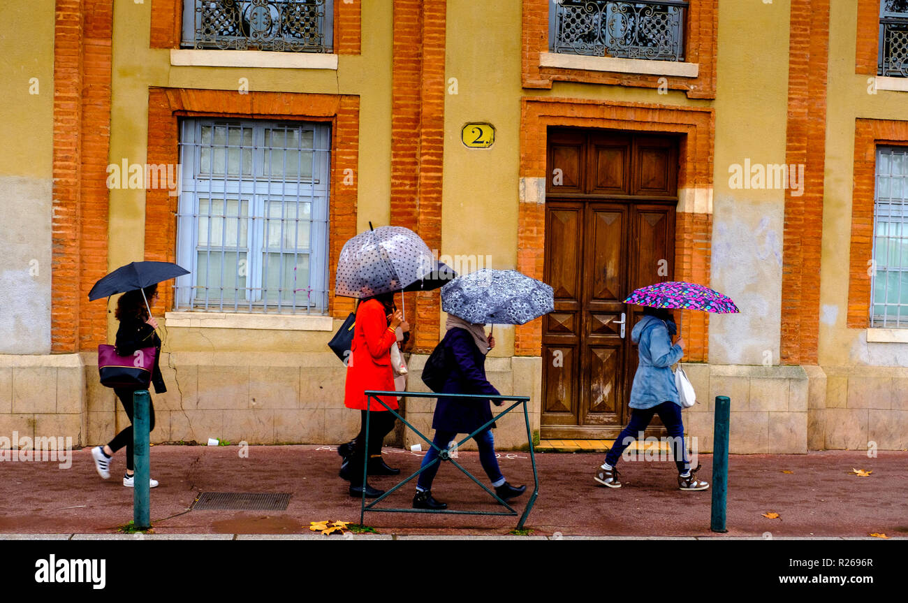 Persone con ombrelloni a piedi sotto la pioggia in Quai Saint-Pierre, Toulouse, Francia Foto Stock