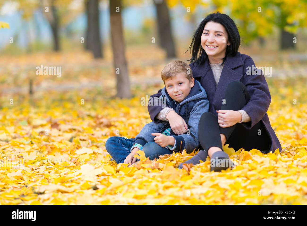 Un felice, contenuto madre e figlio seduti in un parco della città tra giallo Foglie di autunno. Foto Stock