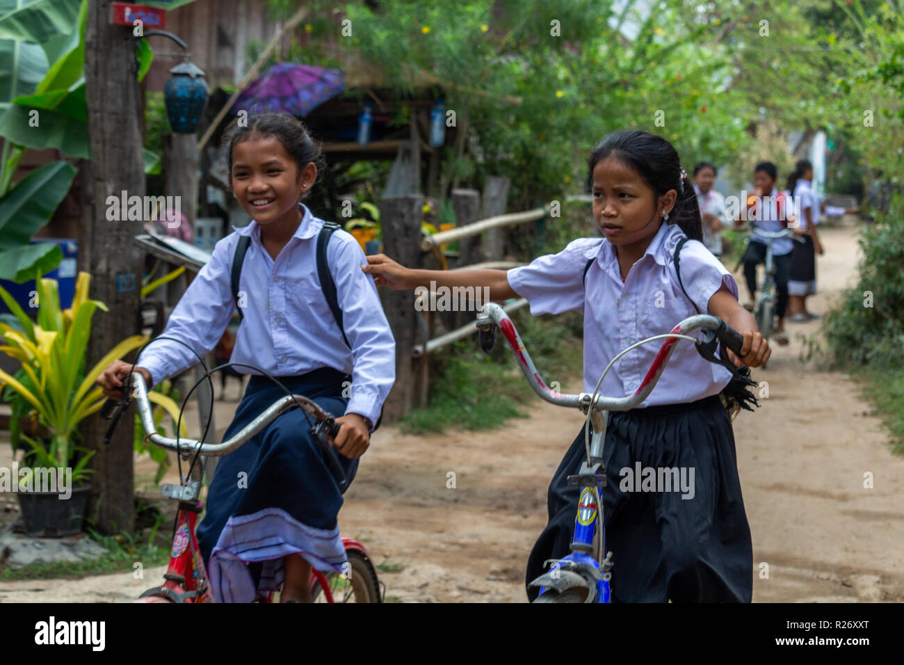 Don Det, Laos - Aprile 24, 2018: scuola locale ragazze tenendo le mani mentre si guida biciclette su una strada fangosa Foto Stock