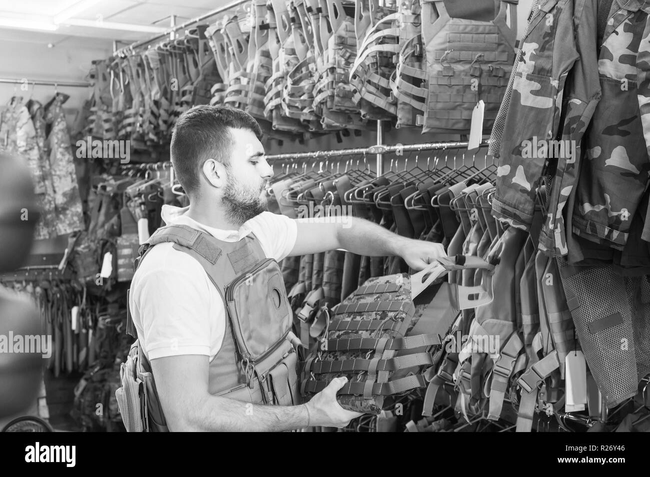 Positivo giovane ragazzo italiano scegliendo flak jacket in negozio militare Foto Stock