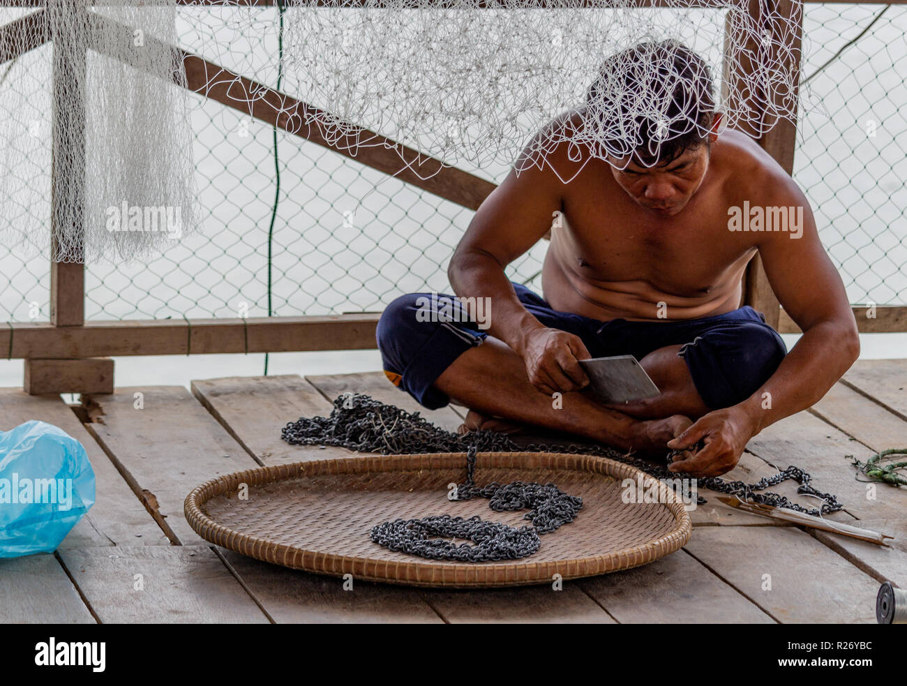 Don Det, Laos - Aprile 24, 2018: pescatore locale riparando il suo metallo equimpent pesca su una terrazza in legno vicino al fiume Mekong Foto Stock