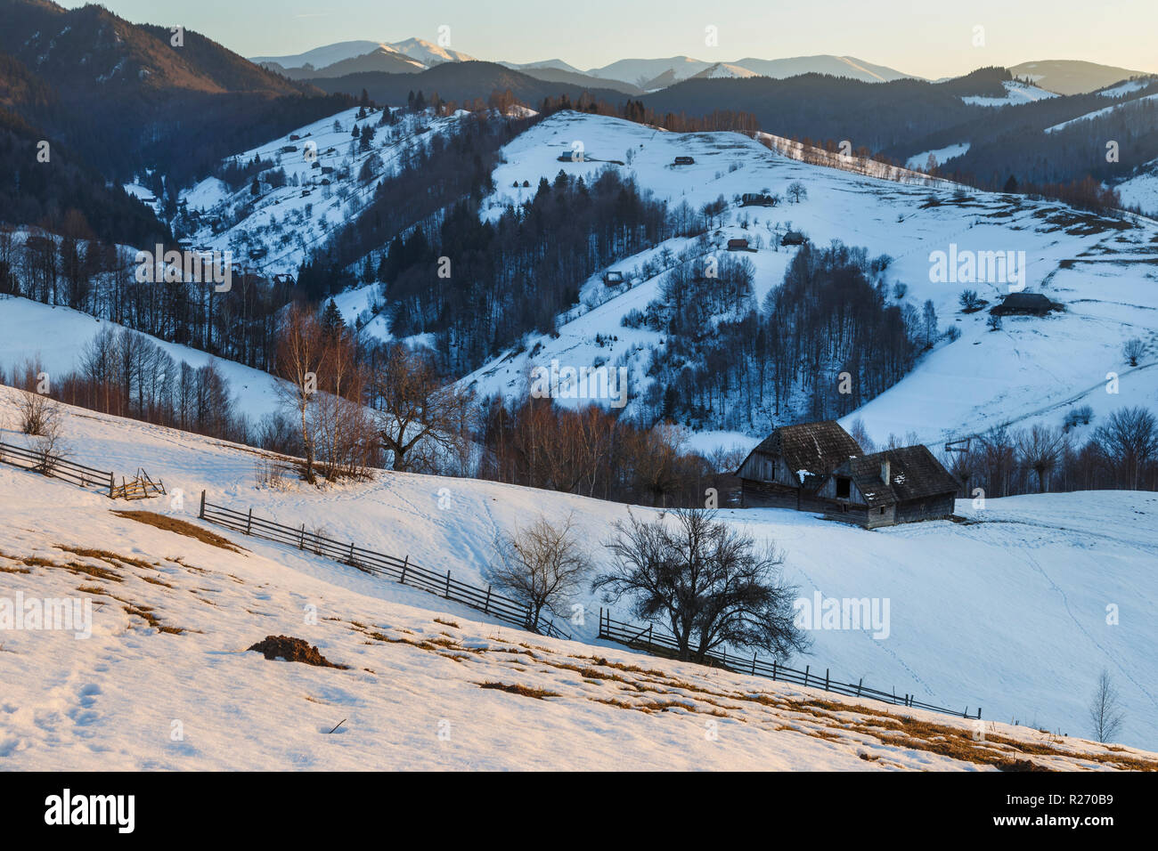 Spettacolare paesaggio invernale. Tramonto in inverno, vecchia montagna rurale chalets in legno e colline innevate vicino a Brasov, Transilvania, Romania Foto Stock