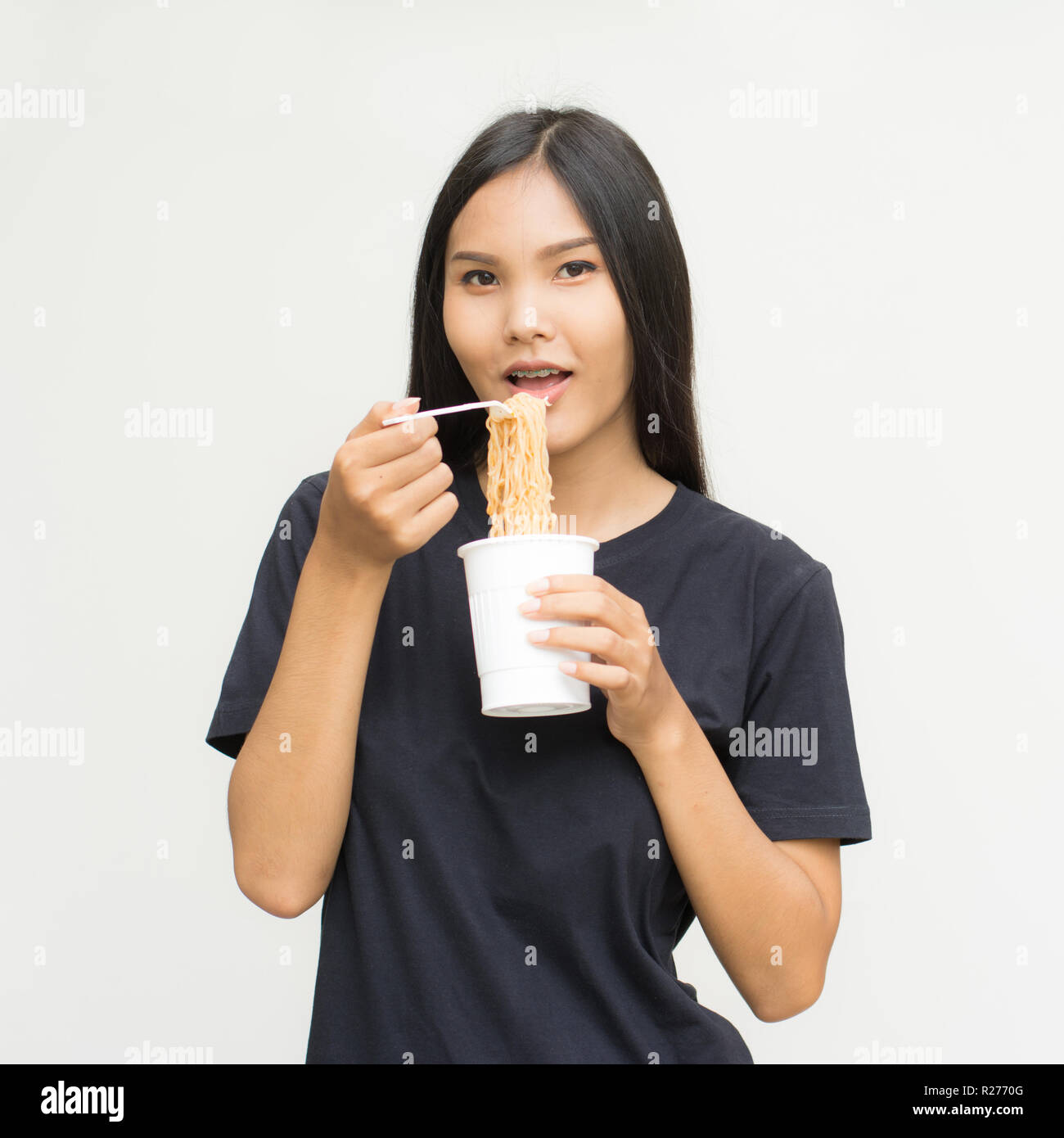 Giovane bella donna asiatica mangiare squisito piccante e speziato a base di noodle istantanei utilizzando bastoncini isolato su sfondo grigio.concetto malsano Foto Stock