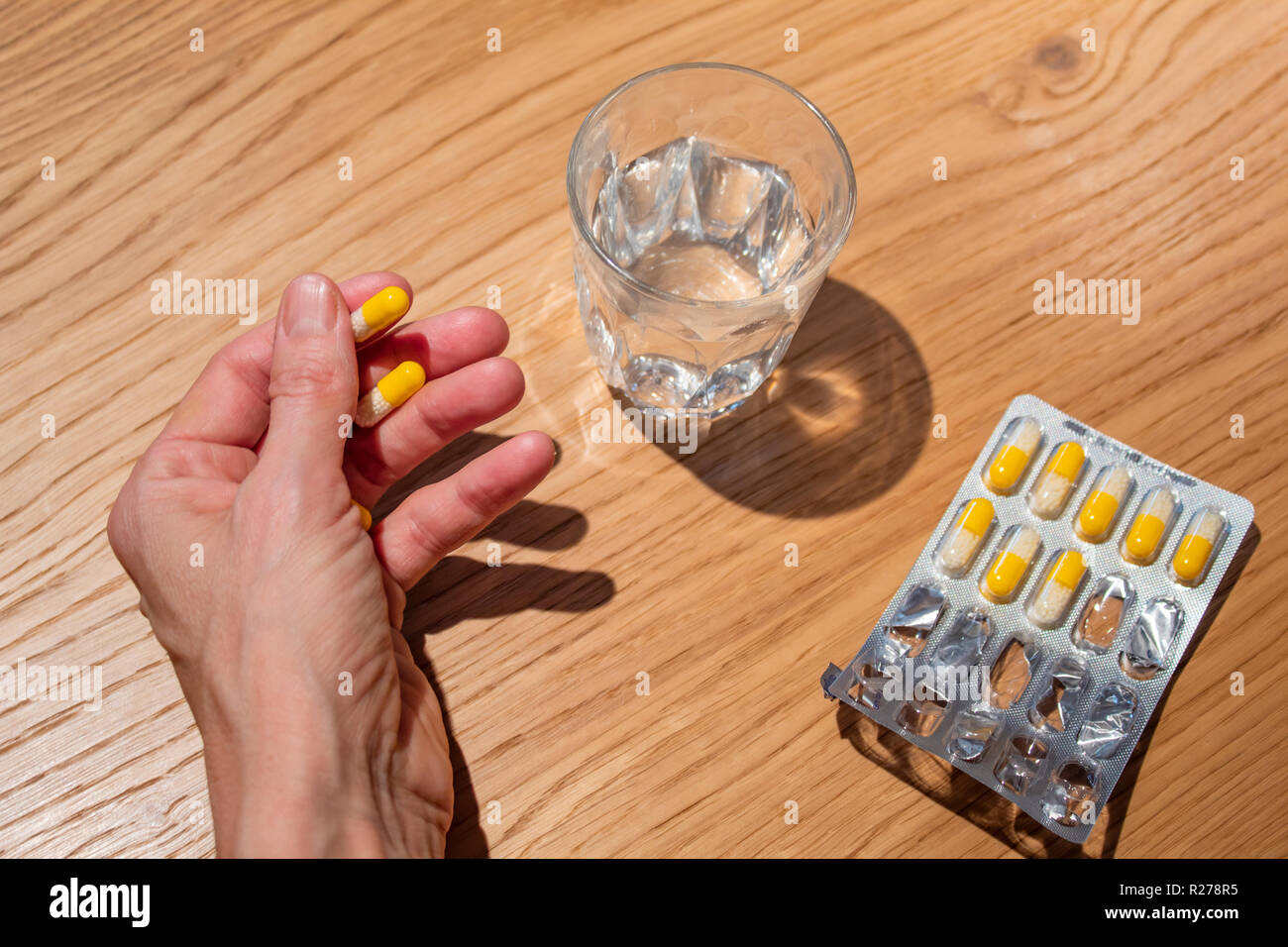 Mano azienda pillole con un bicchiere di acqua e pillole in imballaggi in materie plastiche Foto Stock