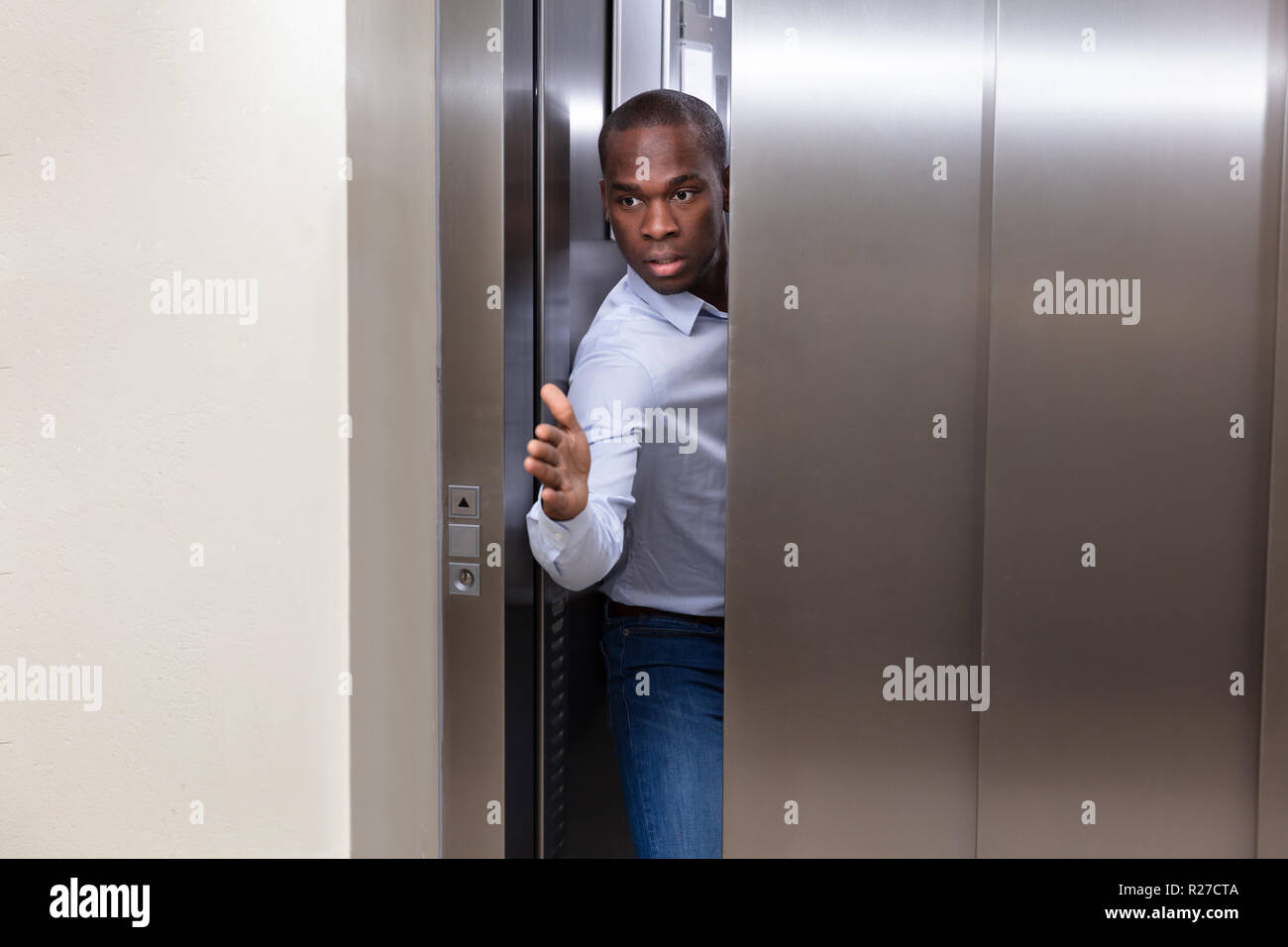 Giovane africano cercando di smettere di ascensore porta con la sua mano Foto Stock