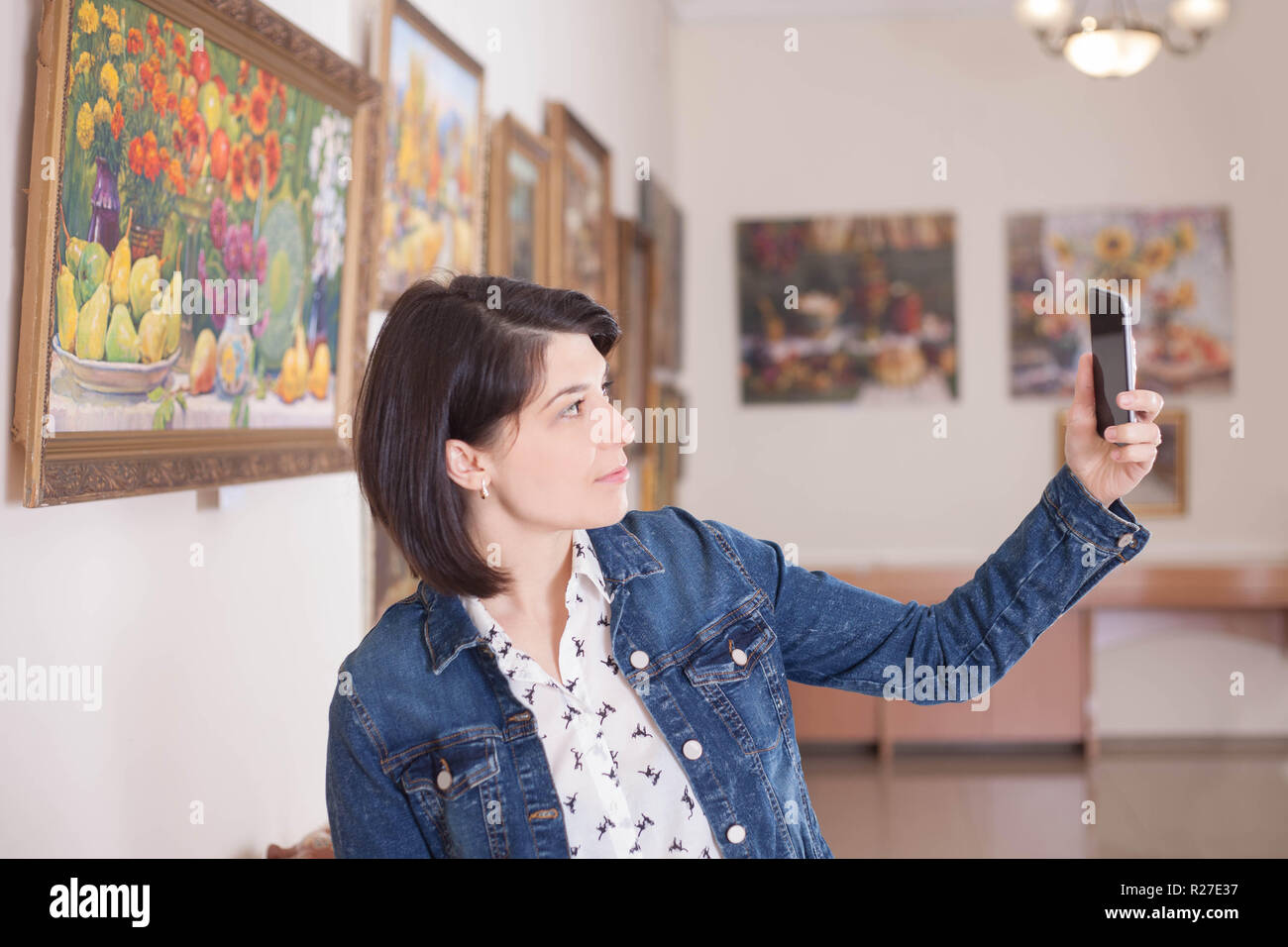 Ritratto di una giovane donna prendendo un selfie in una galleria d'arte o museo. Foto Stock