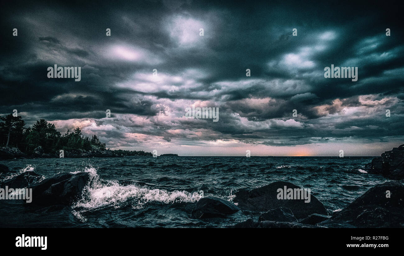 Drammatica Lakeshore nuvole temporalesche. Rappresentazione stilizzata di un oscuro, imponendo il cielo e il tramonto sulla costa rocciosa del lago Superior. Grintoso sfondo vintage. Foto Stock