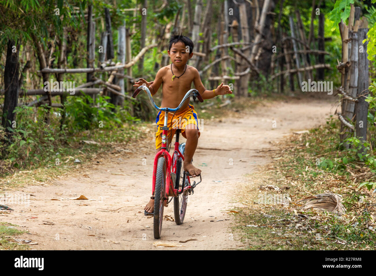 Don Det, Laos - Aprile 24, 2018: ragazzo alla guida di una bicicletta a mani libere su un sentiero circondato da verde nel sud Laos Foto Stock