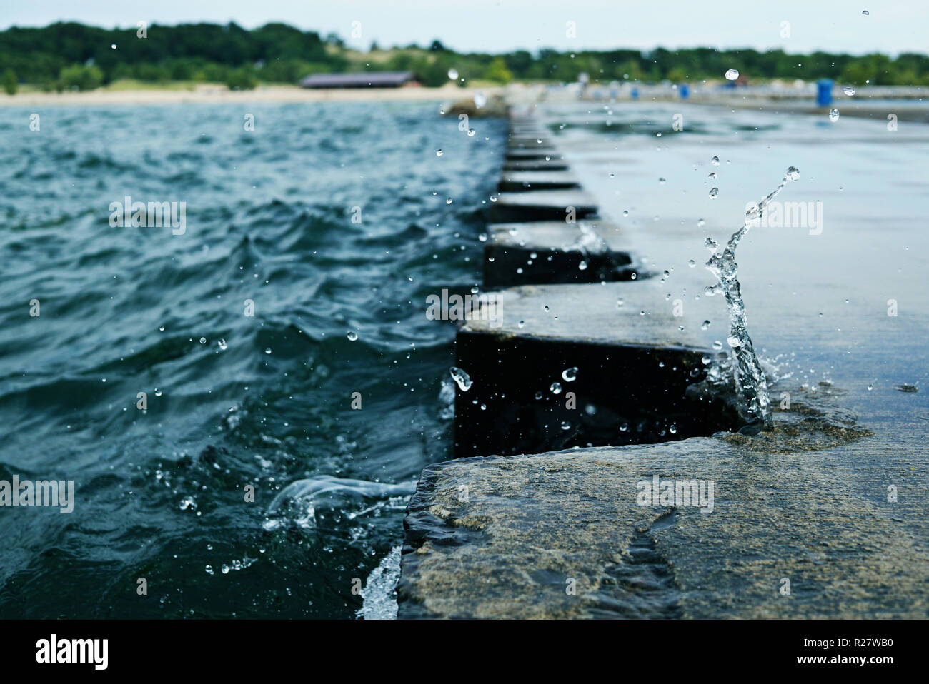 Lo splash di onda su Jetty Pier con colonnine di metallo. Spruzzi di acqua durante la cortina di nubi meteo. Splash si è bloccato sul molo. Stati Uniti d'America, Stato del Michigan, Foto Stock