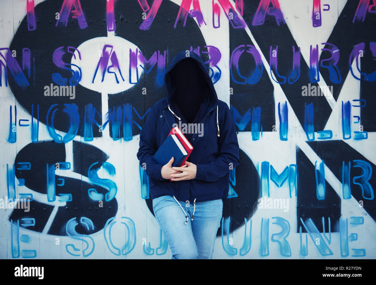 Immagine surreale come donna studente contenere libri e indossando cofano sul volto invisibile lean torna sul muro di graffiti sullo sfondo. Maschera sociale per nascondere il suo id Foto Stock