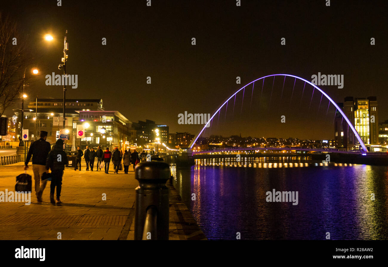 Newcastle Upon Tyne, England, Regno Unito, 17 novembre 2018. Vista dalla banchina del porto con la gente a piedi lungo il Fiume Tyne del pedone Gateshead Millennium Bridge e la Rank Hovis ha Baltic mulino di farina ora Baltic Centre for Contemporary Art pit fino a notte con riflessi nell'acqua Foto Stock