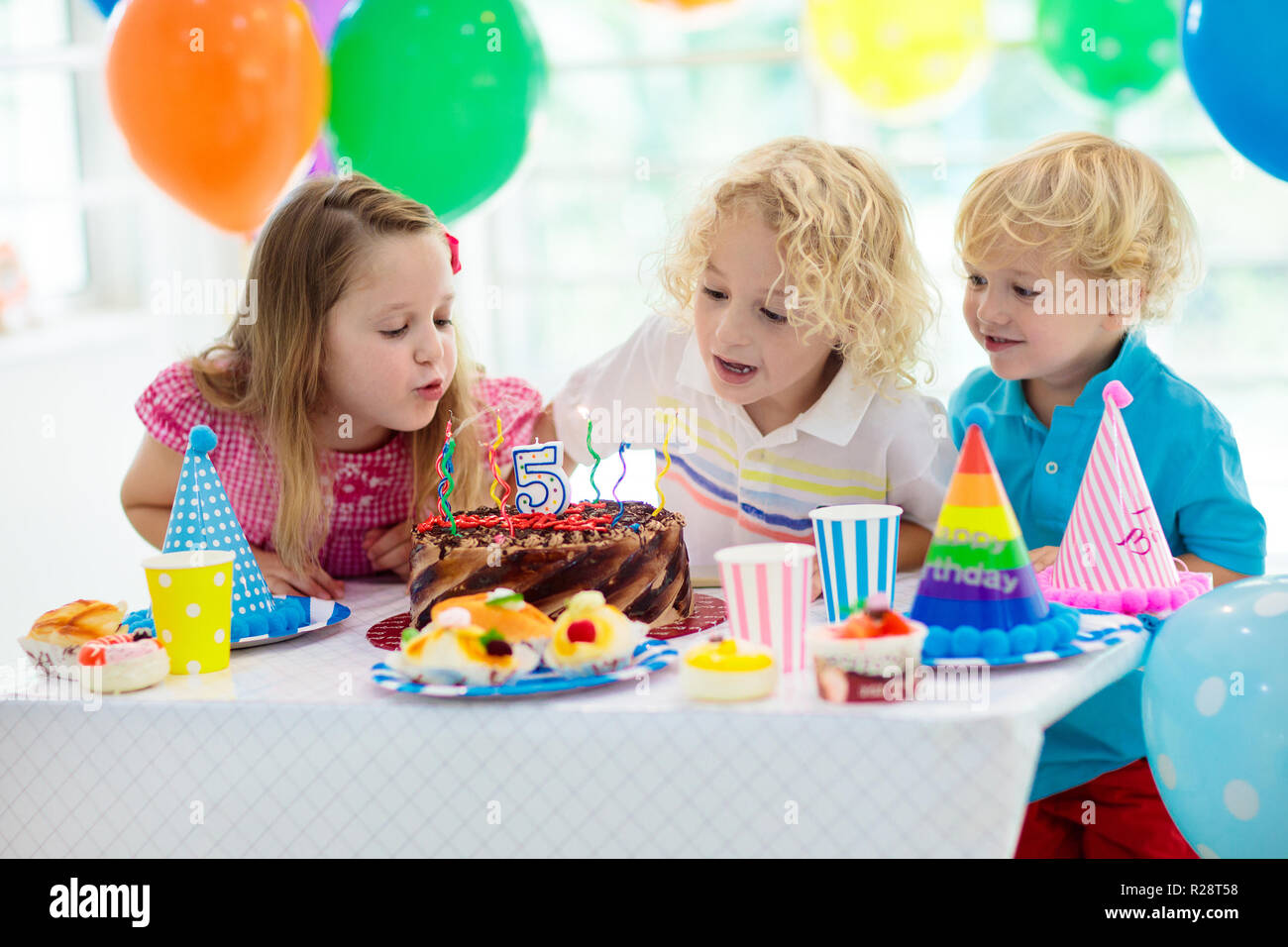 Kids festa di compleanno. Bambino soffiando le candeline sulla torta  colorati. Casa decorata con bandiera arcobaleno banner, palloncini. Animali  da fattoria festa a tema. L Foto stock - Alamy