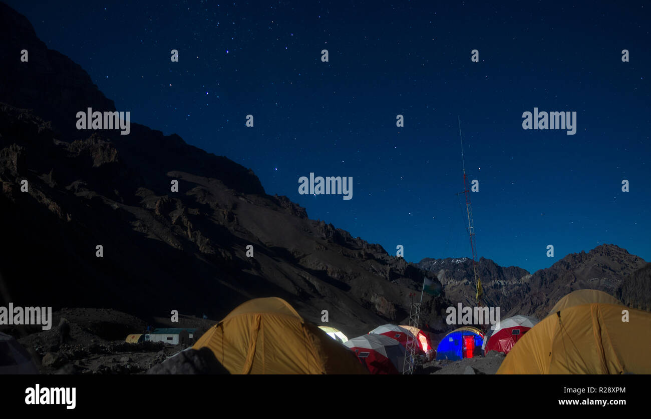 Vista notturna di un accampamento circondato da montagne rocciose con una notte stellata Foto Stock