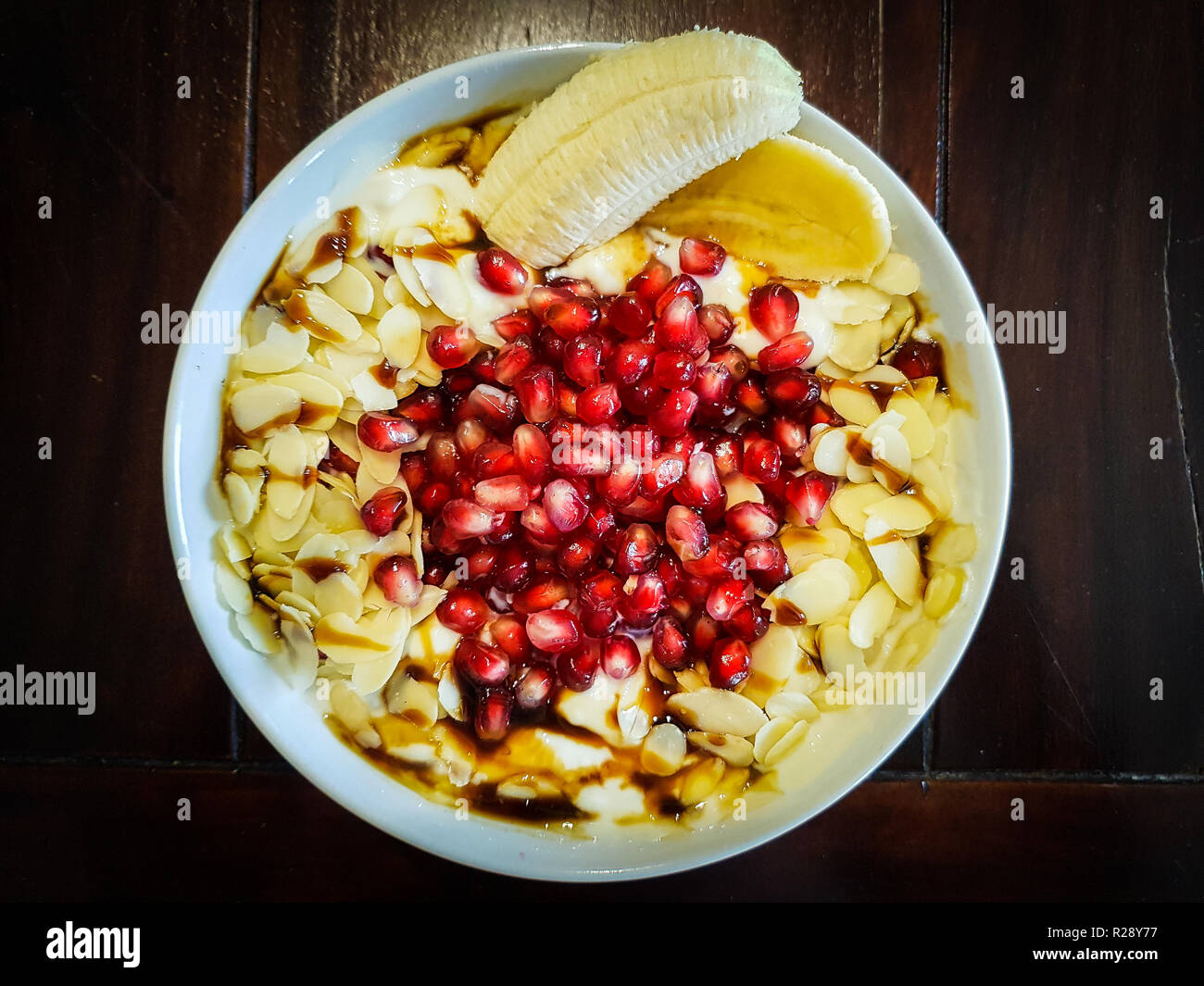 Una ciotola piena di muesli con avena frutti banana mandorle melograno yogurt e sciroppo d'acero Foto Stock