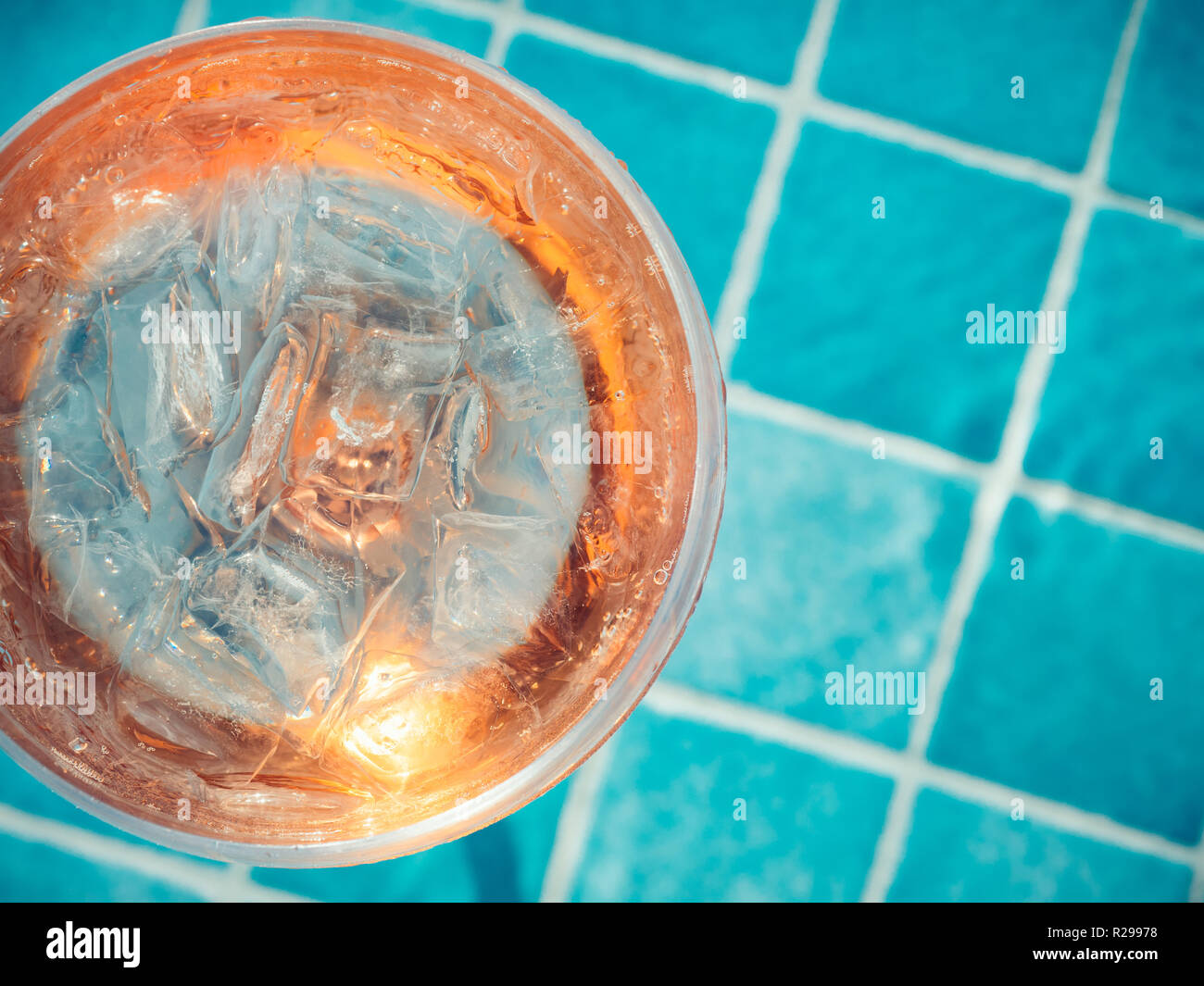 Bellissimo il vetro con un cocktail di rosa e i cubetti di ghiaccio sul  fondo della piscina con acqua blu. Vista superiore, close-up. Riposo  durante una crociera sul mare Foto stock -
