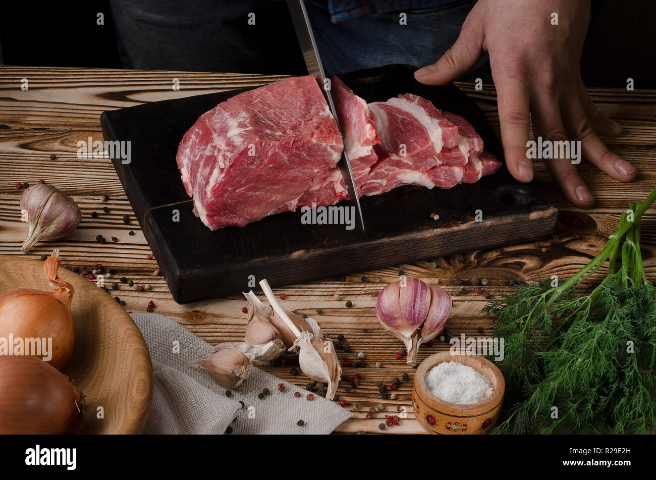 L uomo per affettare la carne di maiale sulla tavola di legno al ristorante  Cucina. Lo chef prepara le carni fresche per la cottura. Moderna cucina  sfondi con verdure Foto stock -