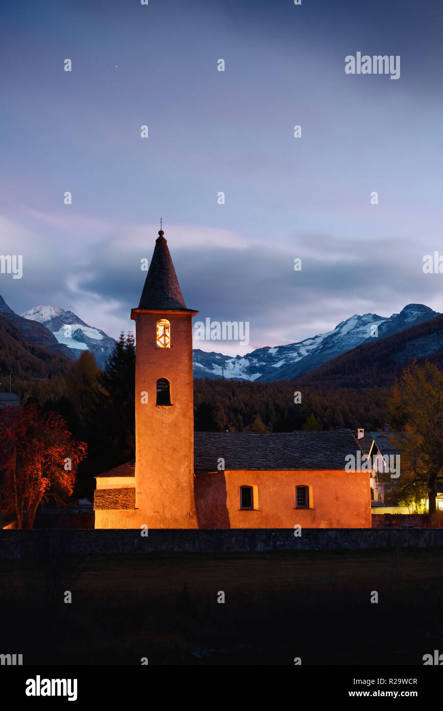 Il cristianesimo chiesa sul villaggio di Sils (vicino al lago di Sils) nelle Alpi Svizzere. Spia arancione sulla costruzione e montagne innevate sullo sfondo. Svizzera Foto Stock