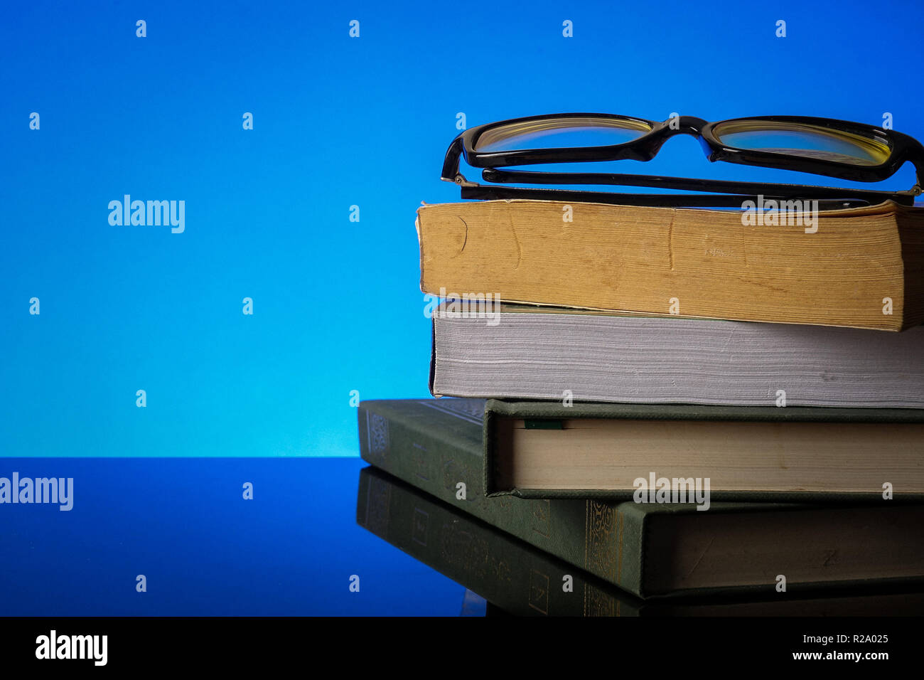 Il concetto di istruzione con la pila di vecchio libro e gli occhiali da lettura su uno sfondo blu. Foto Stock