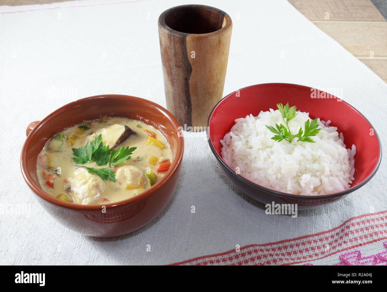 Moqueca di pesce e peperoni, cibo brasiliano, servito con riso bianco su un tavolo di legno. Foto Stock