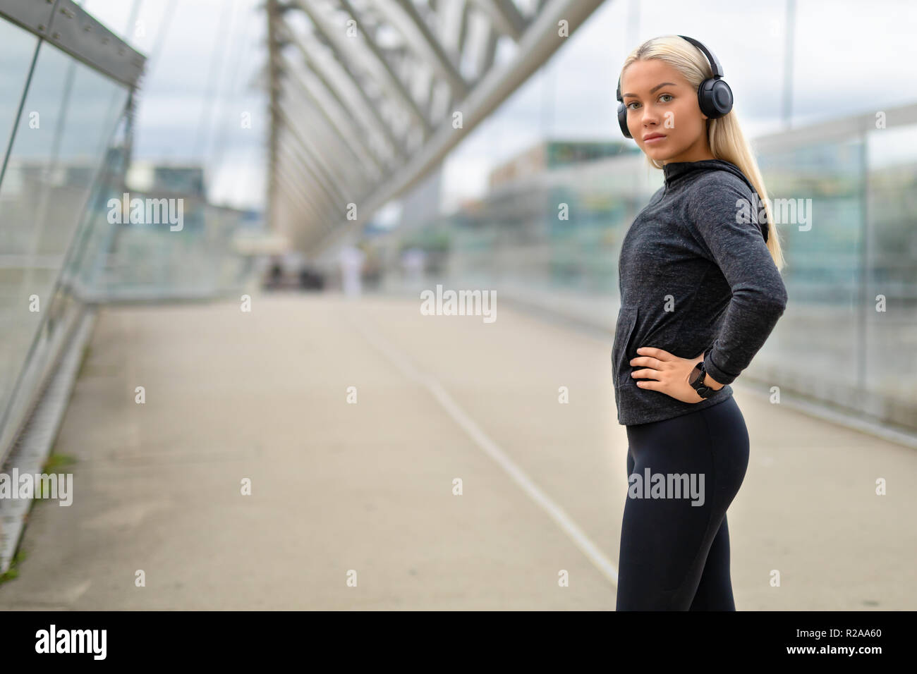 Donna sorridente in nero vestito di allenamento Ascoltare musica sulle cuffie Foto Stock