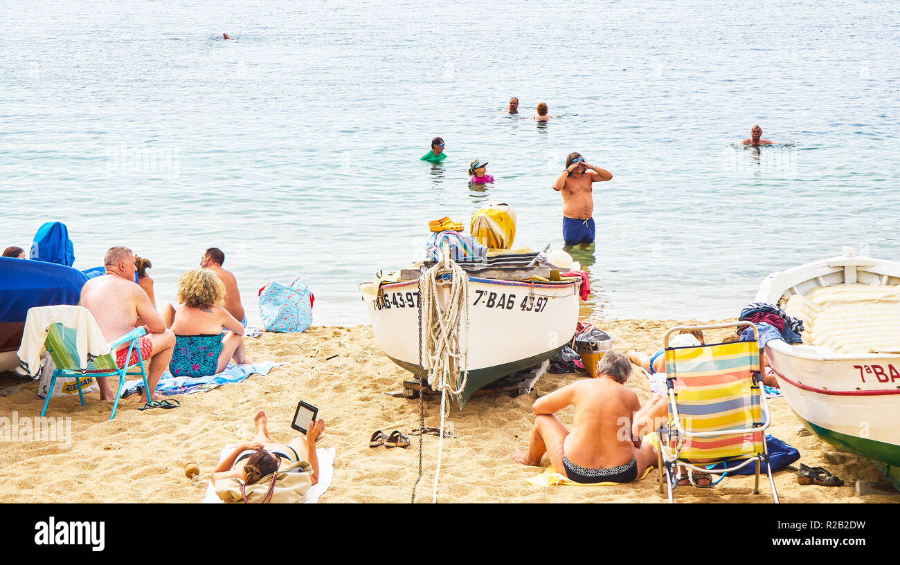 Turisti che si godono una tintarella in Platja de les Barques, una spiaggia di Calella de Palafrugell, Girona Costa Brava Catalogna. Foto Stock