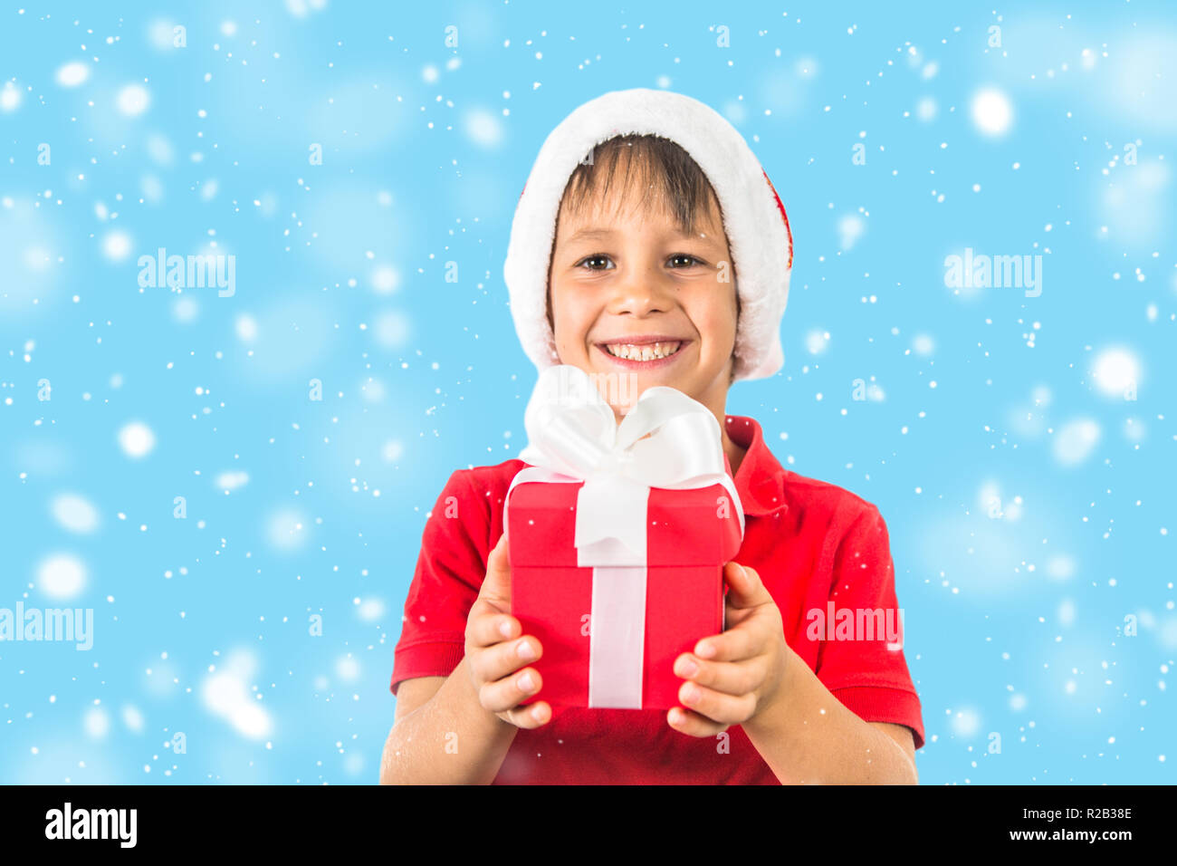 Bambino ragazzo in Christmas Santa hat e rosso presente sulla scatola bianca. Foto Stock