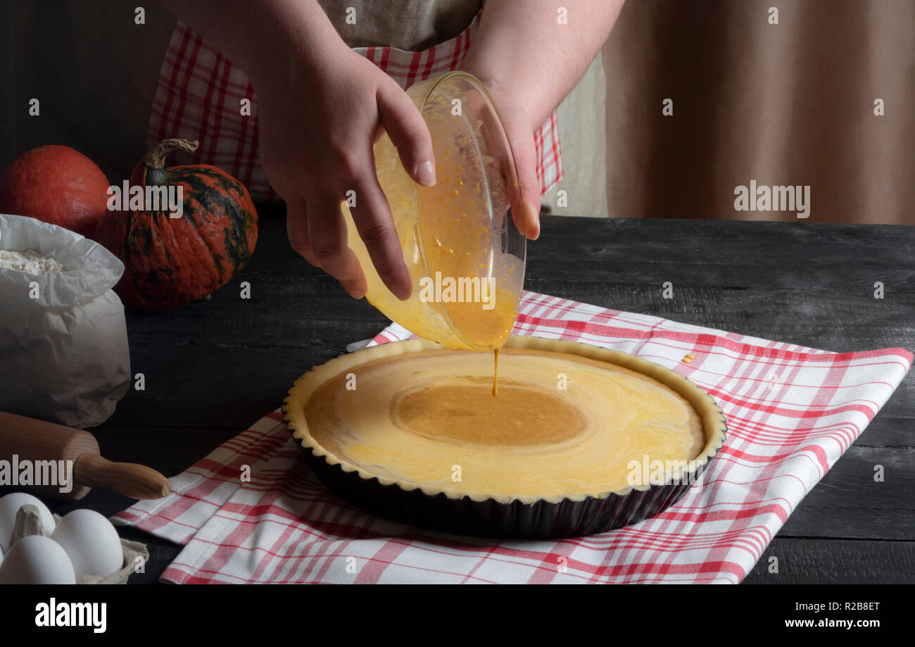 Donna mani di colata di riempimento a torta da una vaschetta in un vassoio con pasta, circondato da ingredienti per la torta di zucca. Classica torta dolce la cottura. Foto Stock