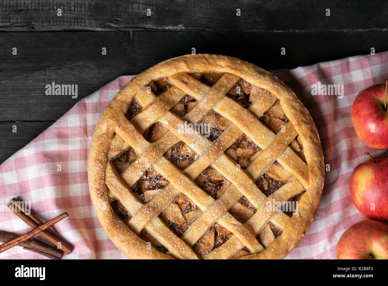 Tavolo rustico con tutta una classica torta di mele su una rosa di carta asciugatutto, circondato da frutta mela e cannella. Vista sopra. In casa dolci da forno. Foto Stock