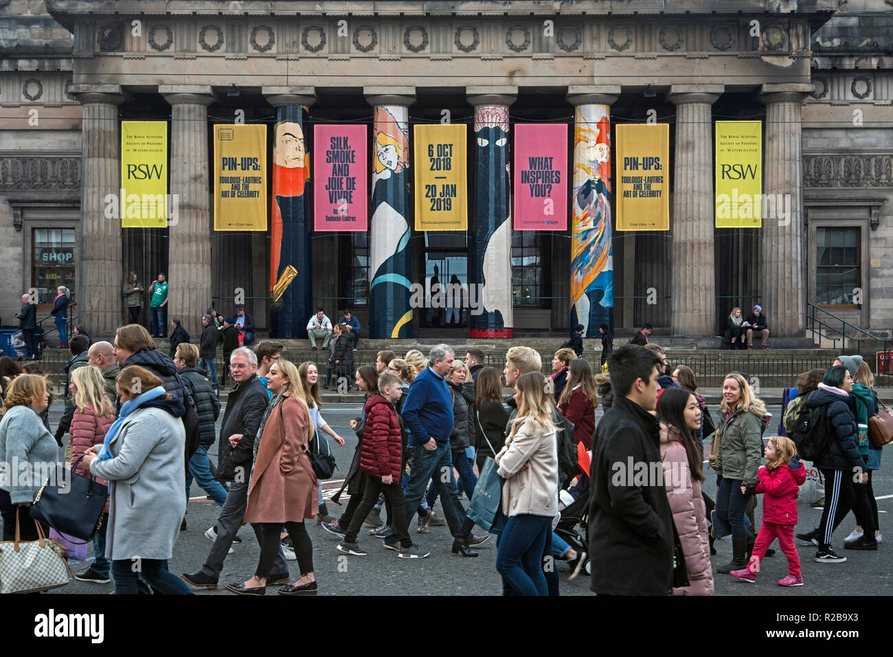 I pedoni a piedi lungo Princes Street di fronte all'edificio RSA pubblicità 'Pin-Ups | Toulouse-Lautrec e l'arte di celebrità' . Foto Stock