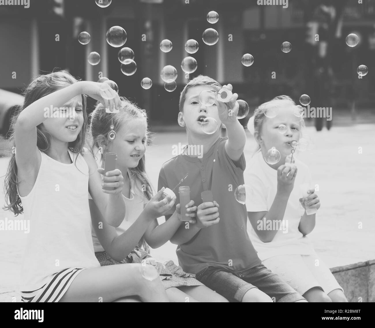 Quattro sorridente i bambini in età scolare seduti insieme e soffiare bolle di sapone Foto Stock