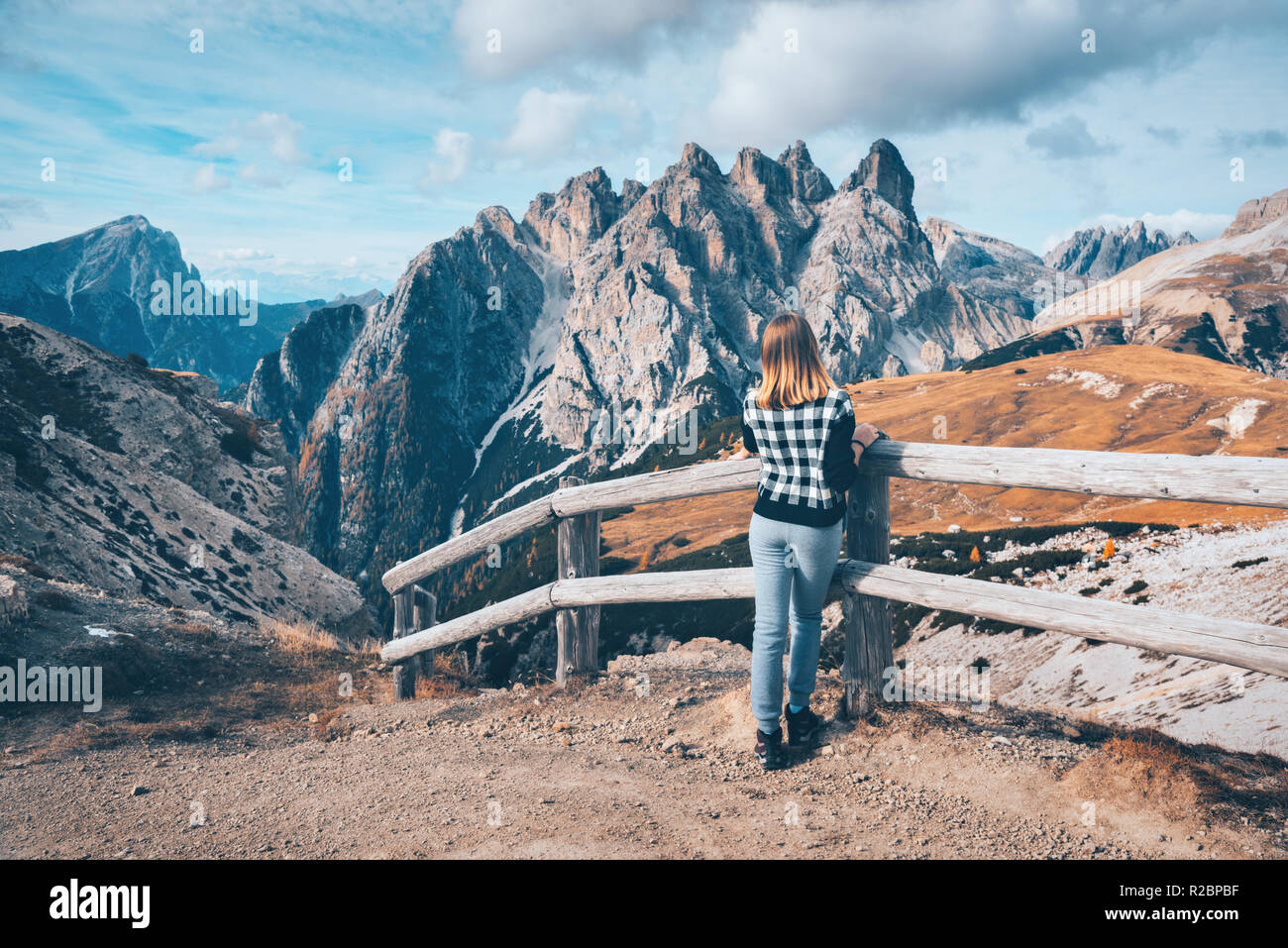 Giovane donna sul sentiero è alla ricerca sulle maestose montagne al tramonto in autunno nelle Dolomiti, Italia. Paesaggio con ragazza, cielo nuvoloso, arancio, erba alta Foto Stock