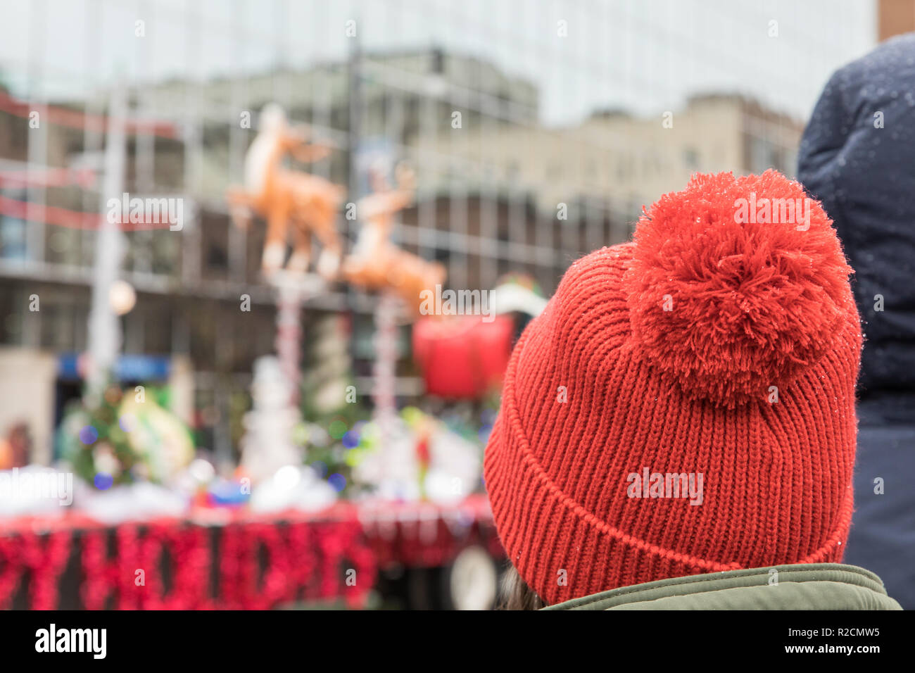Una donna che indossa un rosso pom pom hat orologi una Santa sleigh galleggiante in una sfilata di vacanza Foto Stock