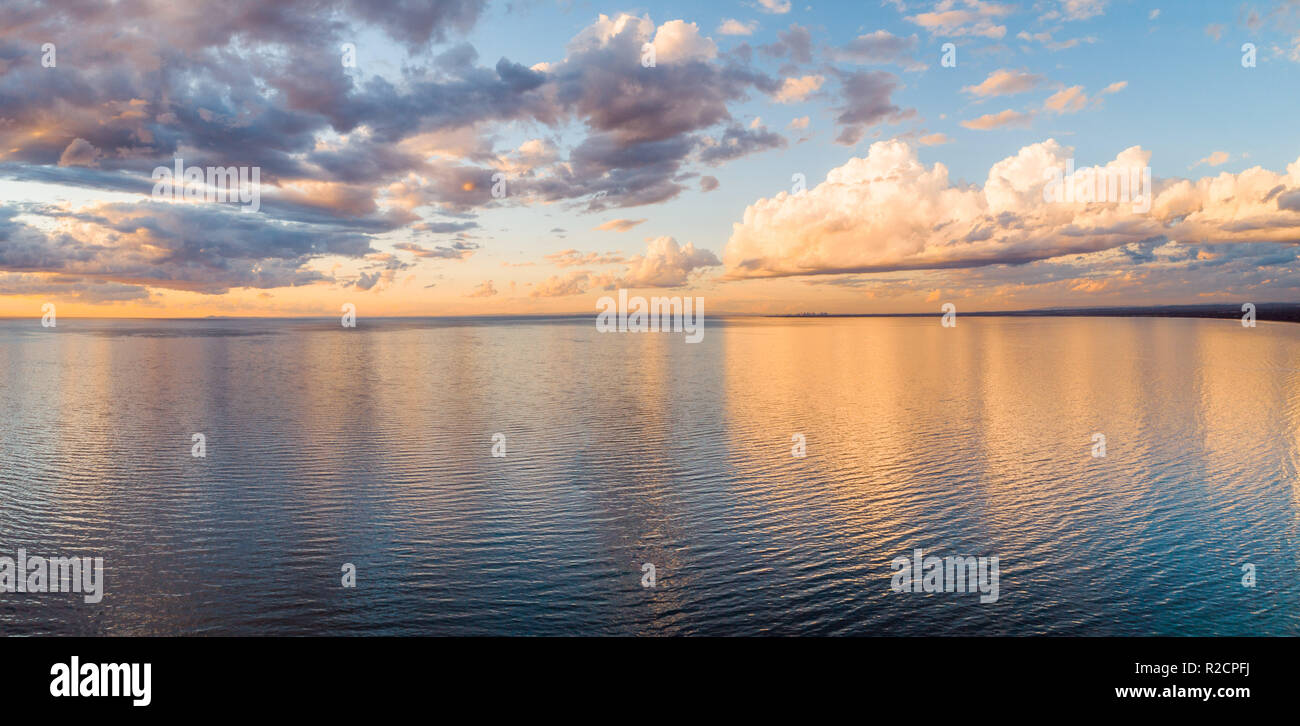 Le nuvole riflettono in mare calmo al tramonto dorato - antenna minimalista panorama Foto Stock