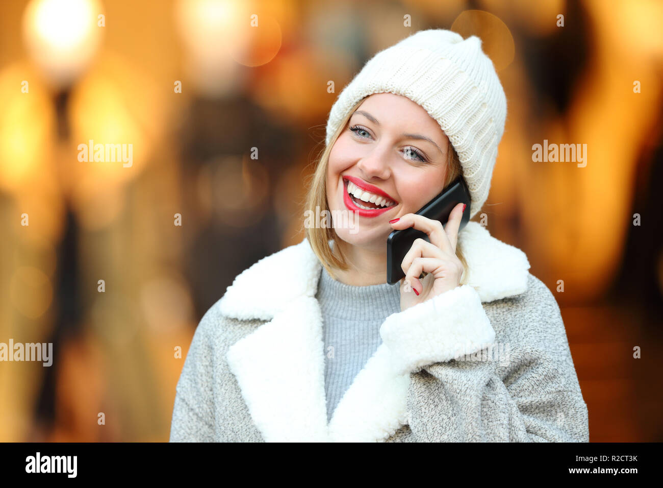 Donna felice di parlare al telefono in inverno in piedi in un centro commerciale Foto Stock