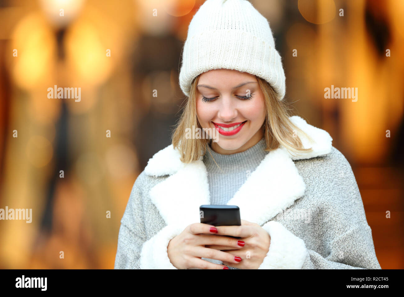 Vista frontale il ritratto di una donna felice utilizzando un telefono intelligente in un centro commerciale di inverno Foto Stock