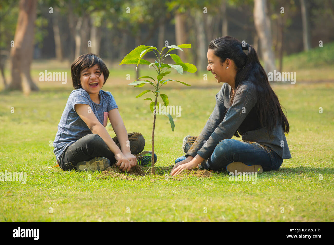 Sorridente fratello e sorella di piantare un piccolo stabilimento in giardino e seduto accanto a esso. Foto Stock