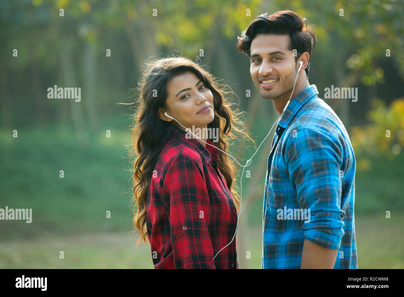 Coppia giovane in piedi in un giardino la condivisione di un auricolare per ascoltare musica. Foto Stock