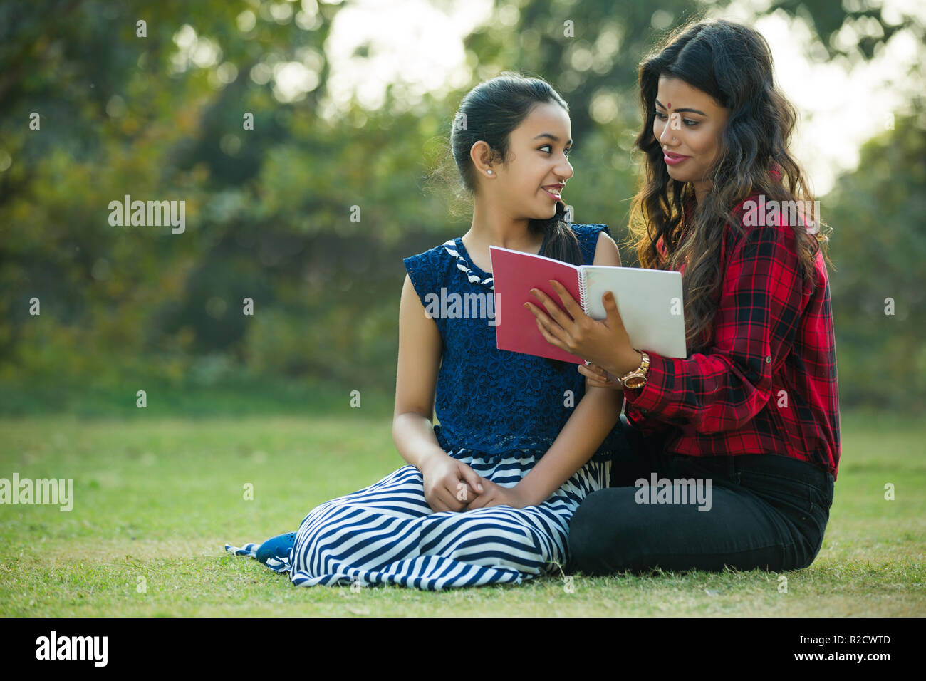 Donna felice e figlia seduti in un giardino guardando ogni altra azienda un libro in mano. Foto Stock