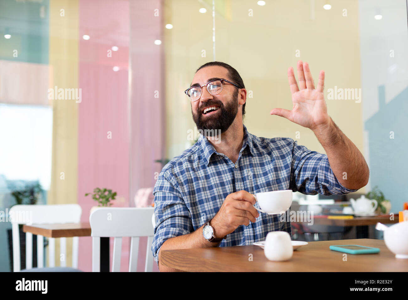 Uomo Barbuto agitando la mano mentre vedere il vecchio amico in cafe Foto Stock