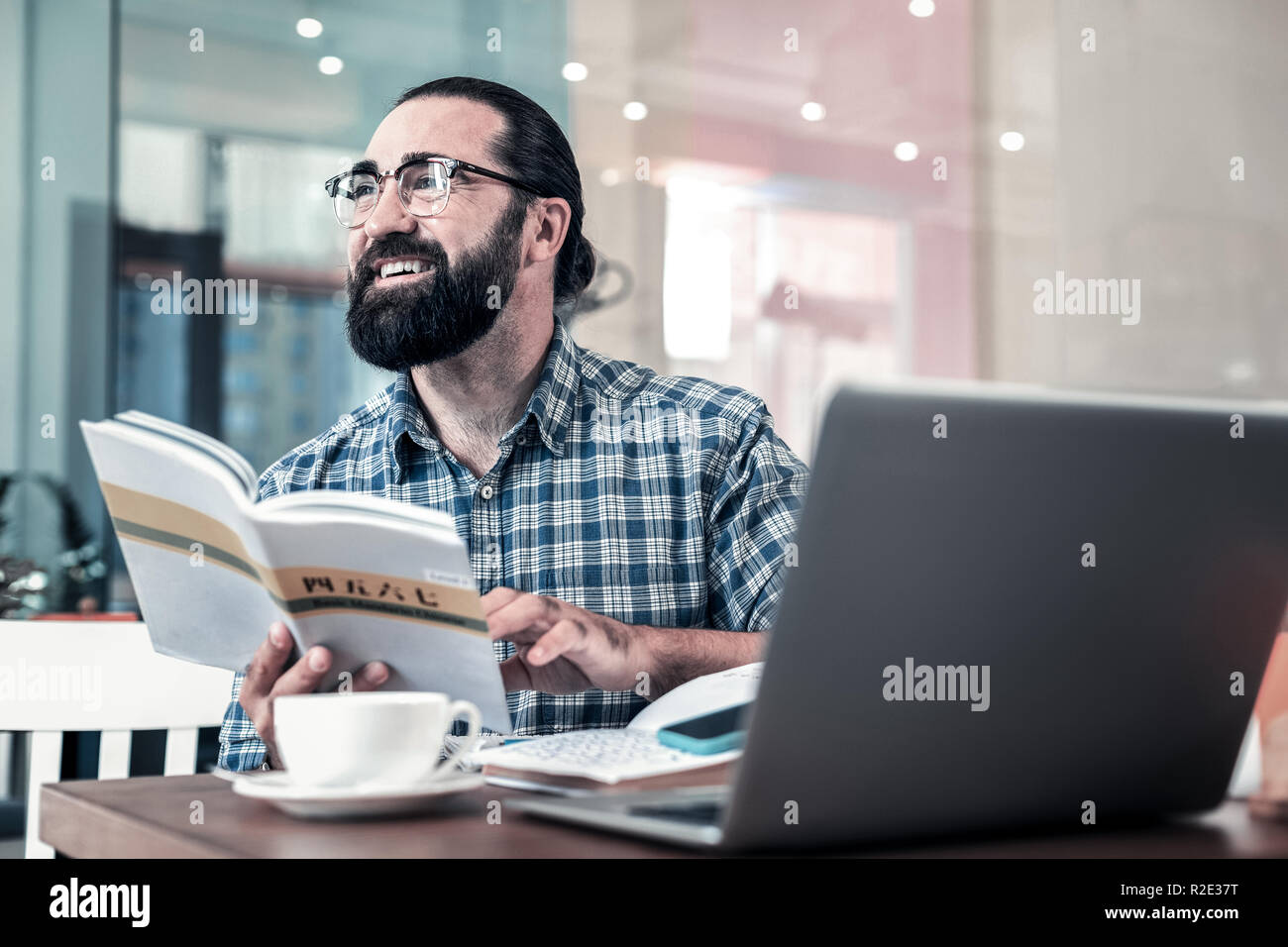 Imprenditore con gli occhiali seduto in un panificio e studiando il cinese Foto Stock