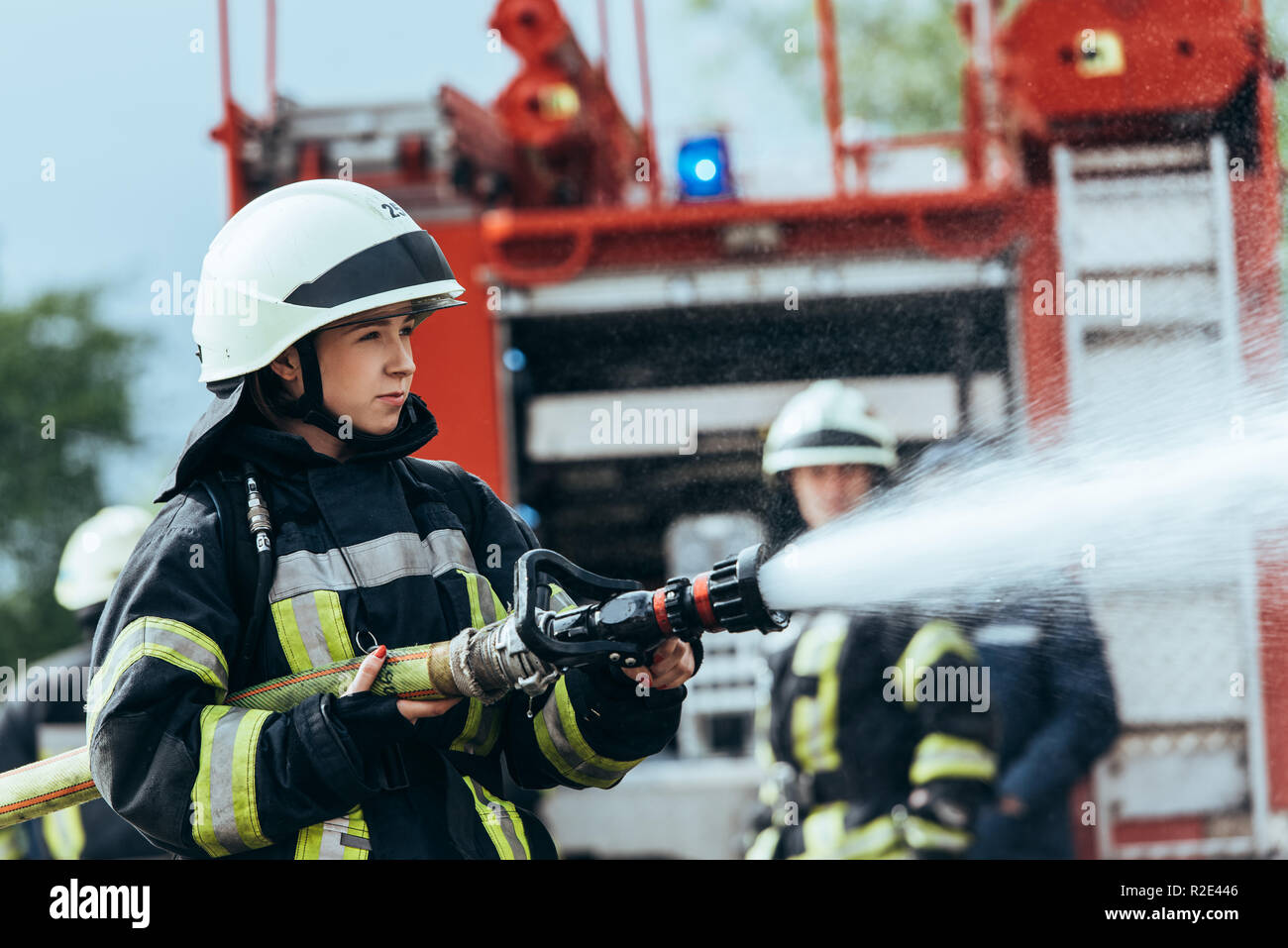 Firefighter femmina con tubo flessibile di acqua di estinguere il fuoco sulla strada Foto Stock