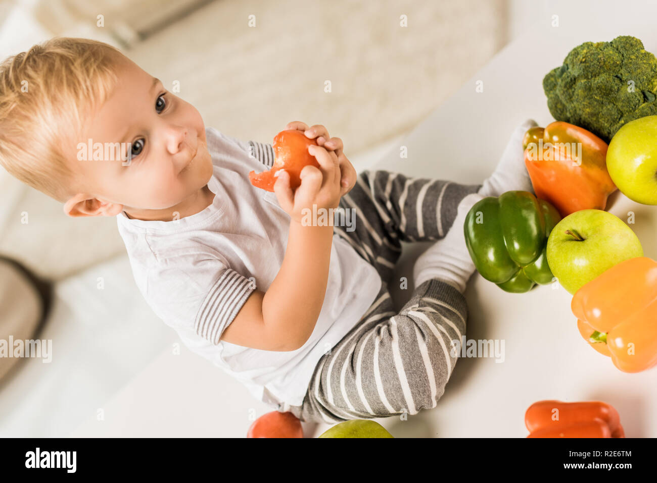 Carino il toddler mangiare e sedersi sul tavolo circondato da frutta e verdura Foto Stock