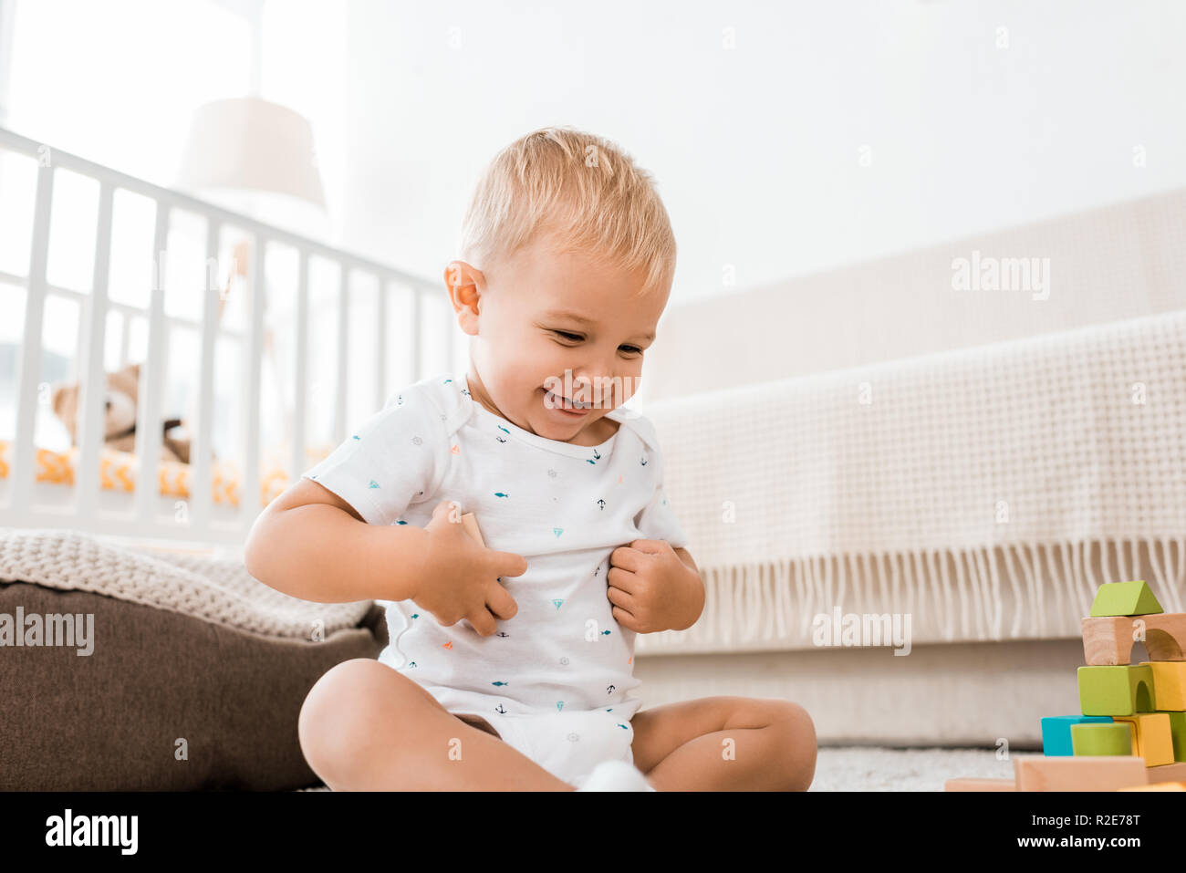 Adorabili toddler sorridente e seduta sul pavimento con cubi colorati in nursery room Foto Stock