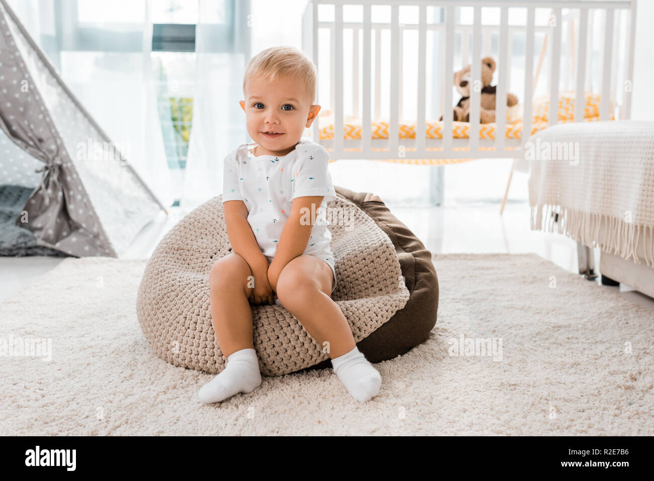 Adorabili toddler sorridente seduto sulla poltrona sacco e guardando la telecamera nella nursery room Foto Stock