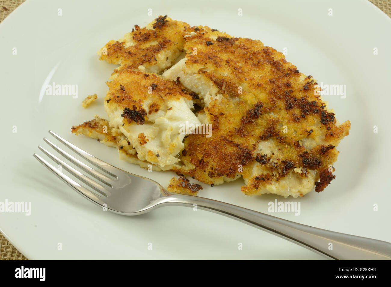 Cotto piccante chipotle impanati tilapia filetto di pesce sulla piastra bianca con forca Foto Stock