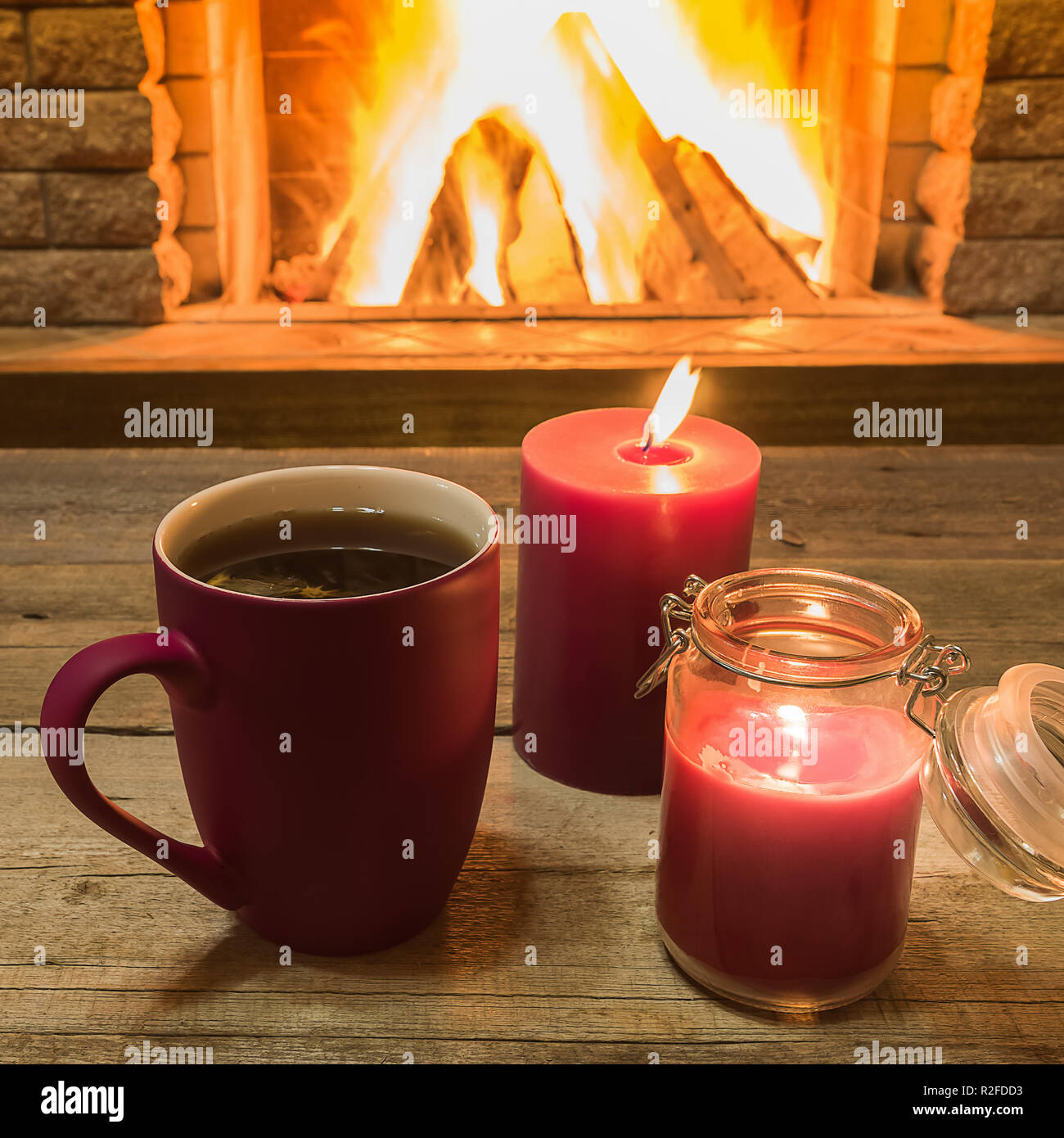 Red cup con un tè caldo e candele , vicino al caminetto, in country house, vacanza invernale, orizzontale. Foto Stock