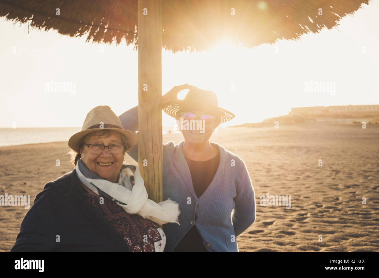 Coppia di anziani di sesso femminile di età compresa in spiaggia durante il tramonto a Tenerife. Concetto di svago per 60s le donne con cappelli e retroilluminazione. Filtro caldo. Foto Stock