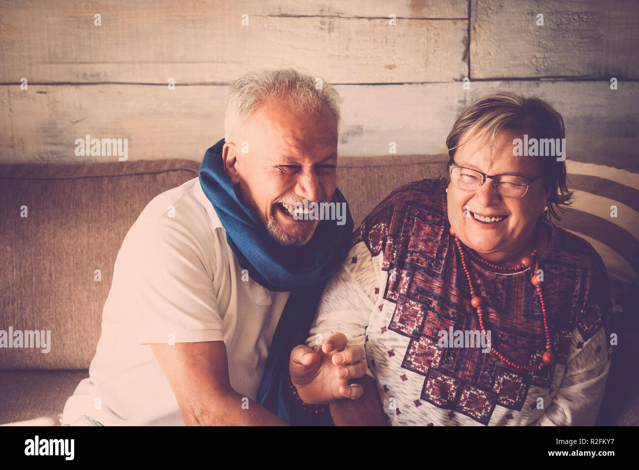 Senior l uomo e la donna con un sacco di divertimento a casa seduti sul divano. Entrambi ridere insieme. Home concetto life. Marrone e colori caldi Foto Stock