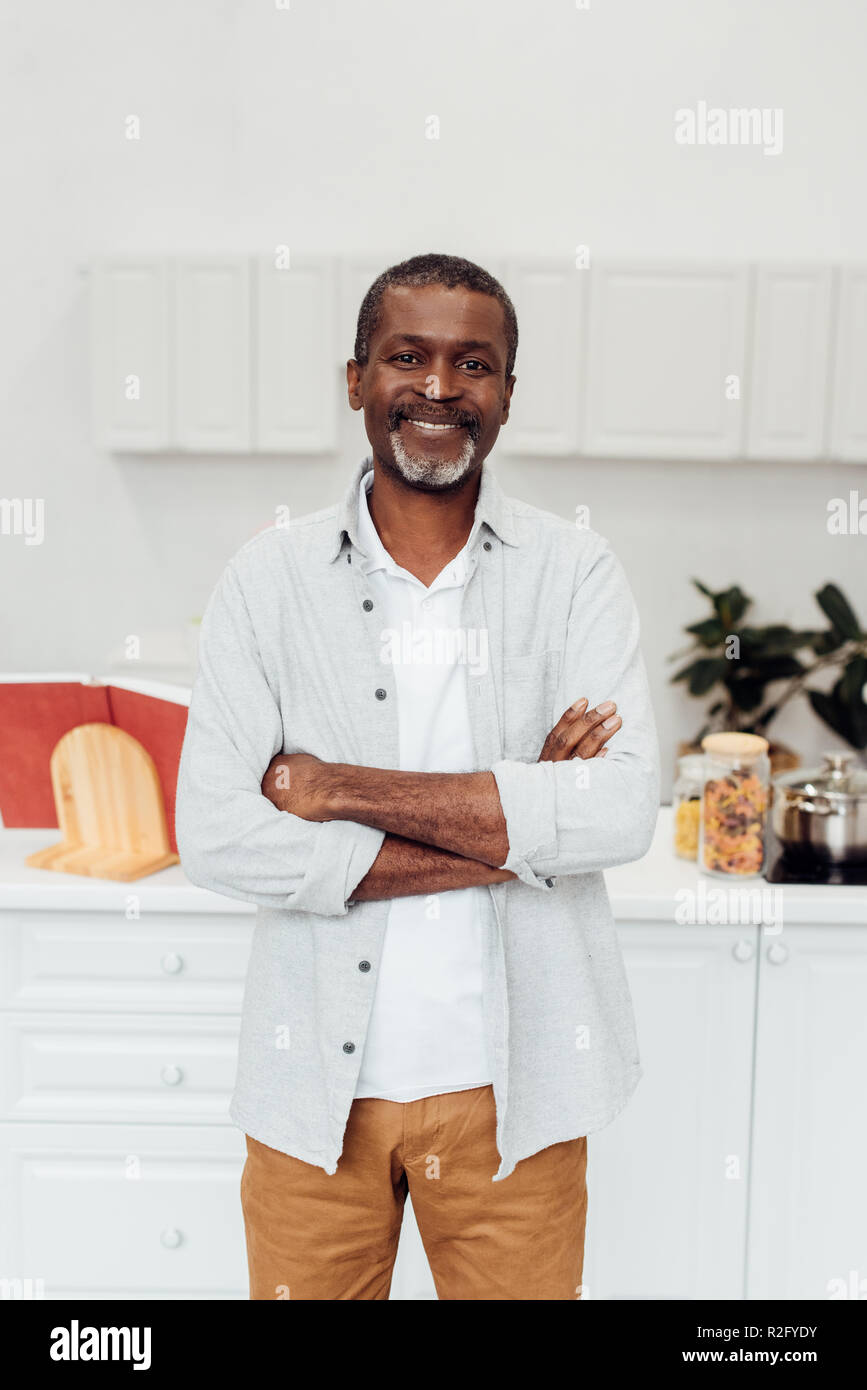 Felice African American uomo maturo con le braccia incrociate in piedi in cucina Foto Stock